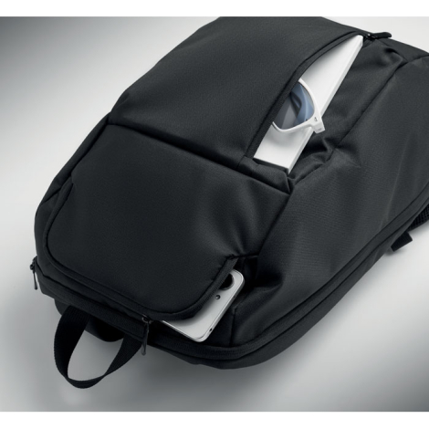 Sac à dos noir posé à plat avec deux poches frontales ouvertes, contenant une paire de lunettes et un smartphone.