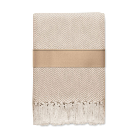 Couverture pliée beige clair à motif chevrons, avec franges sur le bas et manchette en papier kraft autour de la partie centrale