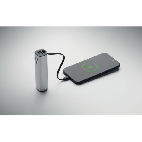 Batterie externe argentée reliée par son câble intégré à un smartphone en cours de charge.