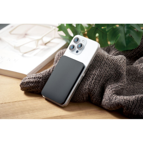 Smartphone blanc posé sur un textile gris avec le powerbank magnétique noir fixé au dos.