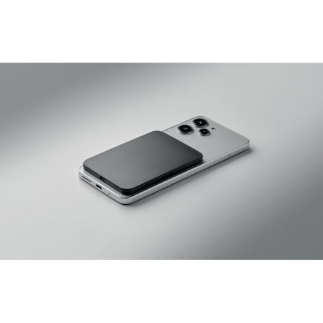 Vue en perspective du powerbank magnétique noir fixé au dos d’un smartphone posé à plat.