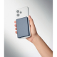 Batterie externe bleu foncé fixée au dos d’un smartphone blanc tenu dans une main. Batterie externe bleu foncé fixée au dos d’un smartphone blanc tenu dans une main.