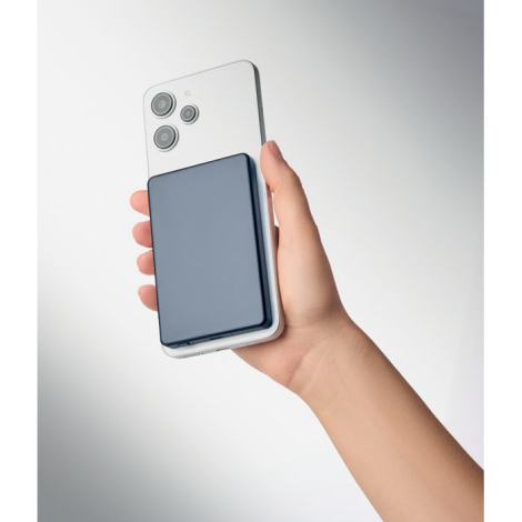 Batterie externe bleu foncé fixée au dos d’un smartphone blanc tenu dans une main.