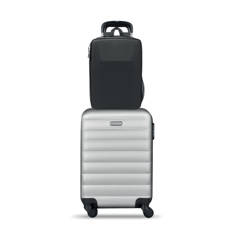 Sac à dos noir installé sur la poignée télescopique d’une valise rigide argentée, illustrant son positionnement sur un bagage à 