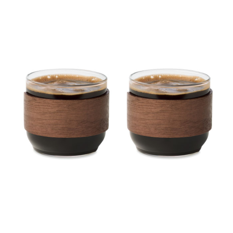 Deux tasses en verre remplies de café, avec leur large poignée en bois entourant la partie centrale.
