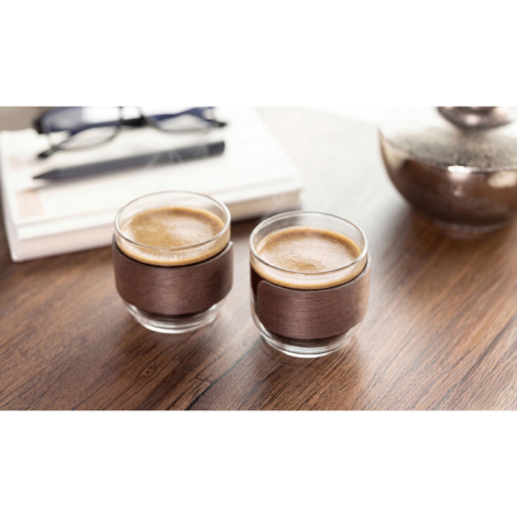 Deux tasses en verre remplies de café sont posées sur une table en bois, à proximité de livres et d’une cafetière.