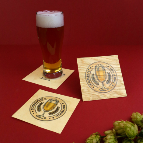 Trois sous-verres carrés en bois clair avec personnalisations imprimées, disposés sur fond rouge. Deux sont posés à plat et un t