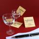 Plusieurs sous-verres carrés en bois clair avec personnalisation noire composée d'un logo et de textes, présentés autour de deux