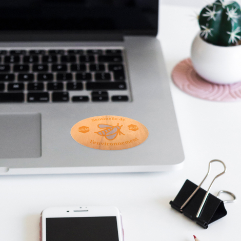 Magnet ovale en bois clair avec veinage apparent et personnalisation orange et grise composée de logos, de textes et d'une illus