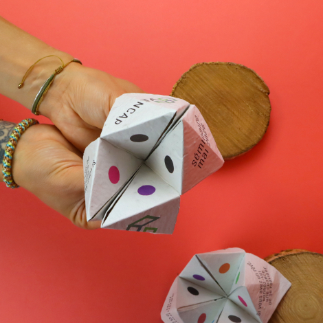 Cocotte en papier personnalisée tenue ouverte dans les mains, avec des pastilles colorées et des textes imprimés sur les rabats,
