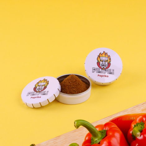 Boîtes rondes à épices personnalisées PILIPILI, contenant du paprika, présentées ouvertes et fermées sur fond jaune avec des poi