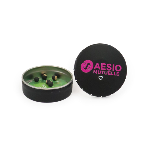 Boîte clic-clac ronde noire personnalisée AESIO Mutuelle, présentée ouverte avec des graines de pois de cœur et son couvercle ma