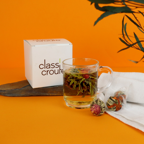 Coffret de thé à fleurs avec boîte personnalisée Class'croute, tasse en verre remplie de thé fleuri et boules de thé, sur fond o