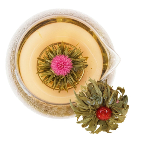 Vue de dessus d'une fleur de thé épanouie avec cœur rose dans une tasse en verre remplie d'infusion dorée, accompagnée d'une sec