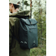 Homme photographié de profil et de dos en forêt, portant un sac à dos noir à rabat, avec deux motifs géométriques clairs sur le 