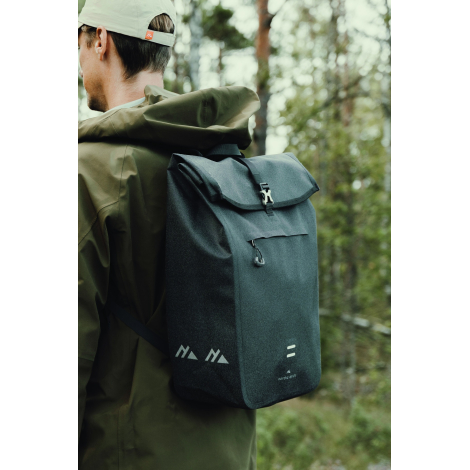 Homme photographié de profil et de dos en forêt, portant un sac à dos noir à rabat, avec deux motifs géométriques clairs sur le 