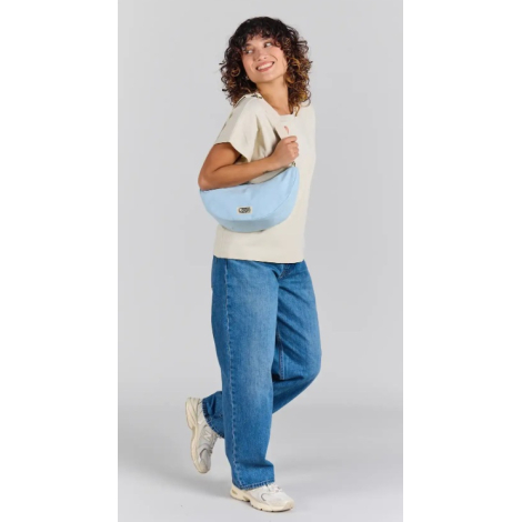 Femme portant à l'épaule le sac lune Inès bleu azur en forme de demi-lune, avec bandoulière écrue réglable et étiquette personna