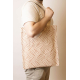 Cabas Nina écru à motifs géométriques orange, porté à l'épaule par un homme, avec longues anses écrues et étiquette frontale.