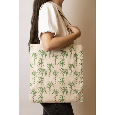 Cabas Nina écru à motifs palmiers verts, porté à l'épaule par une femme, avec longues anses écrues et étiquette rectangulaire su