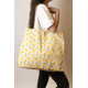 Grand cabas Nina écru à motifs citrons jaunes et feuilles vertes, porté à l'épaule par une femme, avec longues anses écrues et é Grand cabas Nina écru à motifs citrons jaunes et feuilles vertes, porté à l'épaule par une femme, avec longues anses écrues et é