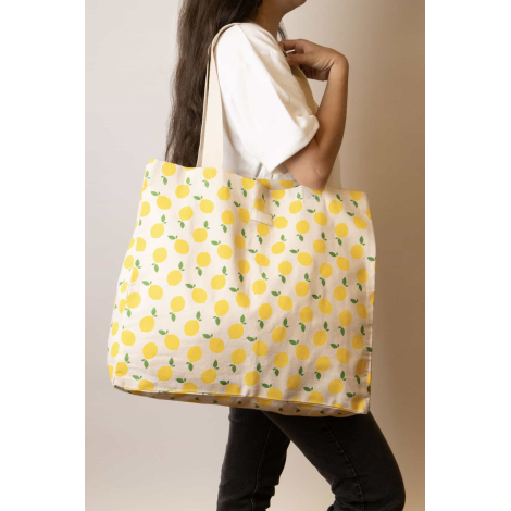 Grand cabas Nina écru à motifs citrons jaunes et feuilles vertes, porté à l'épaule par une femme, avec longues anses écrues et é