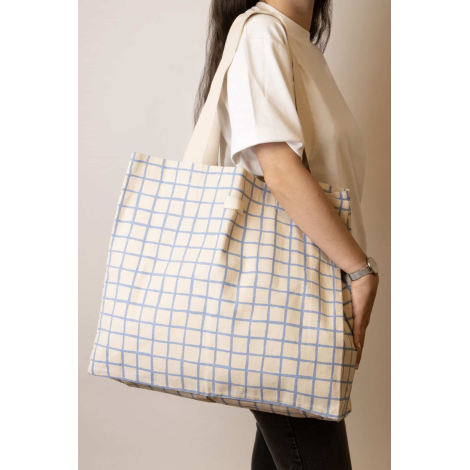Grand cabas Nina écru à motifs quadrillés bleu clair, porté à l'épaule par une femme, avec longues anses écrues et étiquette fro