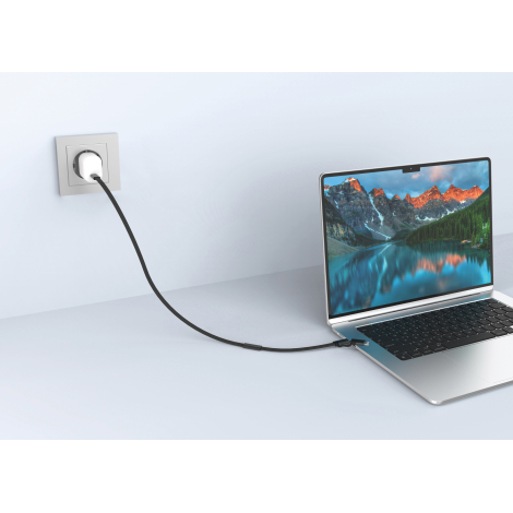 Mise en situation d'un câble de recharge noir reliant un chargeur mural blanc à un ordinateur portable argenté ouvert sur un bur