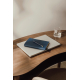 Carnet bleu marine texturé posé sur un ordinateur portable argenté, avec un stylo assorti à détails dorés sur sa couverture. L'e