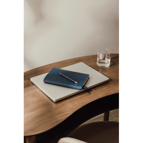 Carnet bleu marine texturé posé sur un ordinateur portable argenté, avec un stylo assorti à détails dorés sur sa couverture. L'e