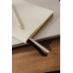Gros plan sur un carnet beige à couverture texturée et tranches dorées, accompagné d'un stylo blanc à pointe dorée. Deux rubans 