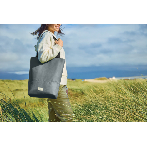 Sac cabas gris porté à l’épaule en extérieur de profil, aucun marquage visible