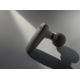 Pistolet de massage noir posé en biais sur surface grise avec jeu d’ombre, neutre sans marquage