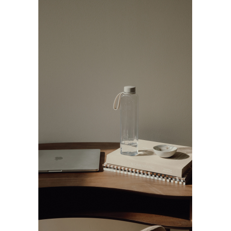 Bouteille translucide claire avec bouchon blanc posée sur des livres