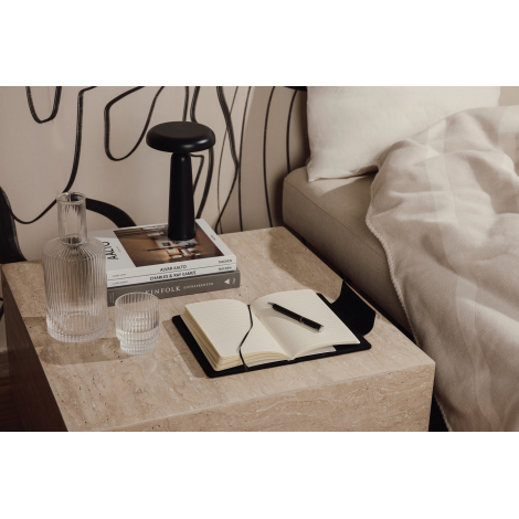 Carnet noir ouvert posé sur une table de chevet à côté d’accessoires