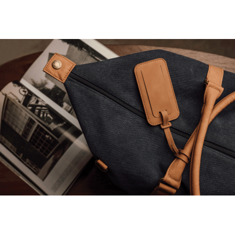 Étiquette bagage attachée à un sac de voyage en tissu bleu foncé. Aucune personnalisation visible.