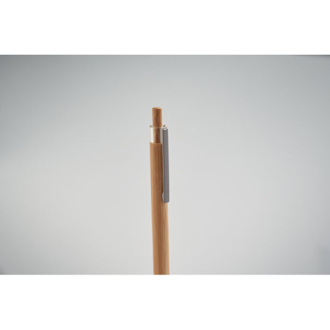 Stylo à bille en bambou gros plan sur le bouton poussoir et clip métallique, sans marquage.