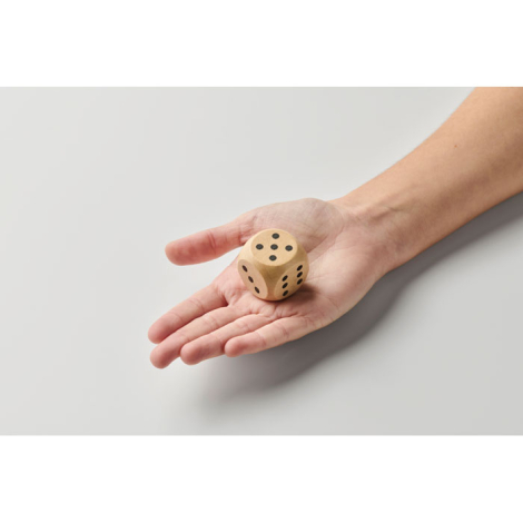 Dé en bois Schima 3 cm tenu dans une main vu de dessus avec plusieurs faces visibles, sans marquage.