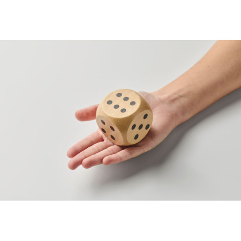 Dé en bois Schima 5 cm tenu dans une main vu de dessus avec plusieurs faces visibles, sans marquage.