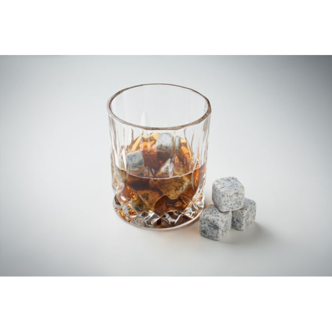 Verre avec boisson ambrée et glaçons en pierre grise, trois glaçons posés à côté.