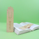 Marque-page en bois posé sur un livre ouvert, gravures visibles sur certains modèles.