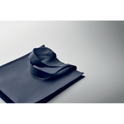 Sac cadeau bleu marine en non-tissé, plié et posé à plat avec anses repliées.