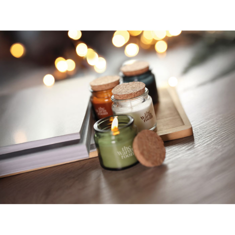 Ensemble de bougies en verre de couleurs variées sur plateau en bois ; bougie verte allumée avec marquage visible sur la face av