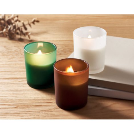 Trois bougies en verre (vert, blanc dépoli, brun) allumées, posées sur une surface en bois.