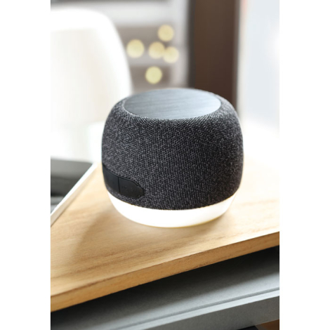 Enceinte ronde avec base blanche posée sur une surface en bois dans un intérieur lumineux.