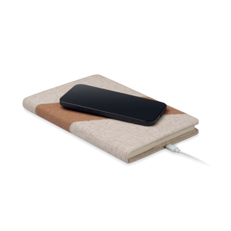 Carnet A5 beige avec bande diagonale en liège servant de station de charge sans fil ; smartphone noir posé sur la couverture, câ