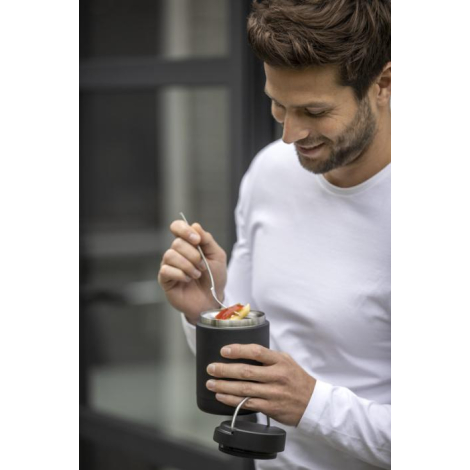 Homme tenant une boîte-repas noire ouverte, dégustant son repas avec une cuillère.