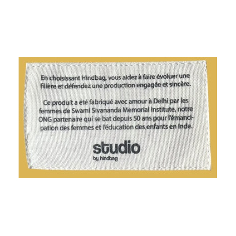 Étiquette blanche cousue sur fond jaune uni, texte noir.