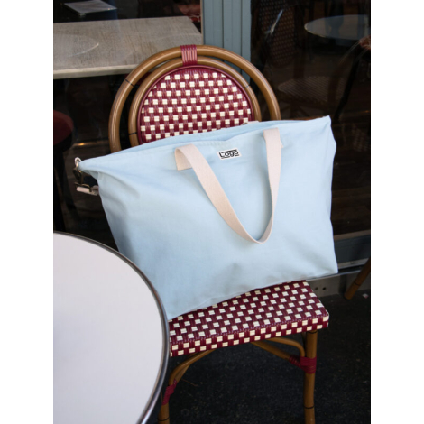 Sac bleu clair posé sur chaise à motif tressé, marquage face avant.