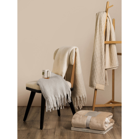 Plaids aux teintes naturelles disposés sur une chaise et un porte-serviettes dans un intérieur chaleureux ; aucune personnalisat