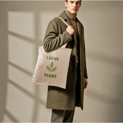 Tote bag beige porté à l’épaule par un homme, illustrant la surface de marquage au dos ; aucune personnalisation visible.